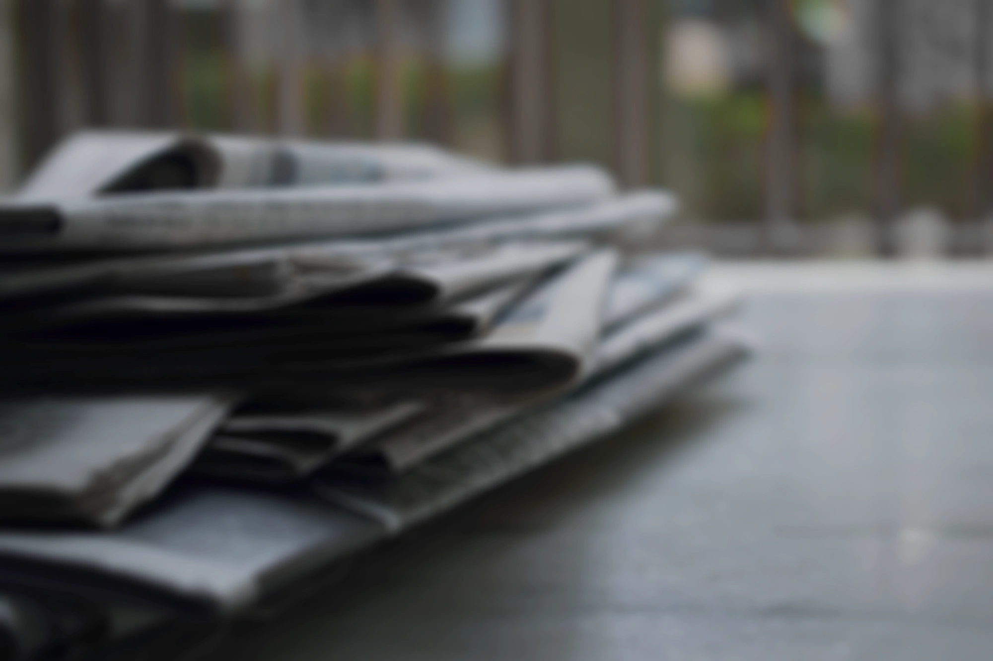 A stack of newspapers on a table with a blurred background.