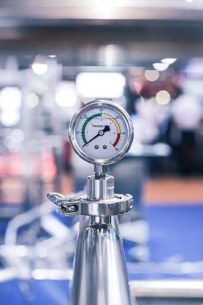 Close up of a pressure gauge on a metal cylinder with blurred gym equipment in the background.