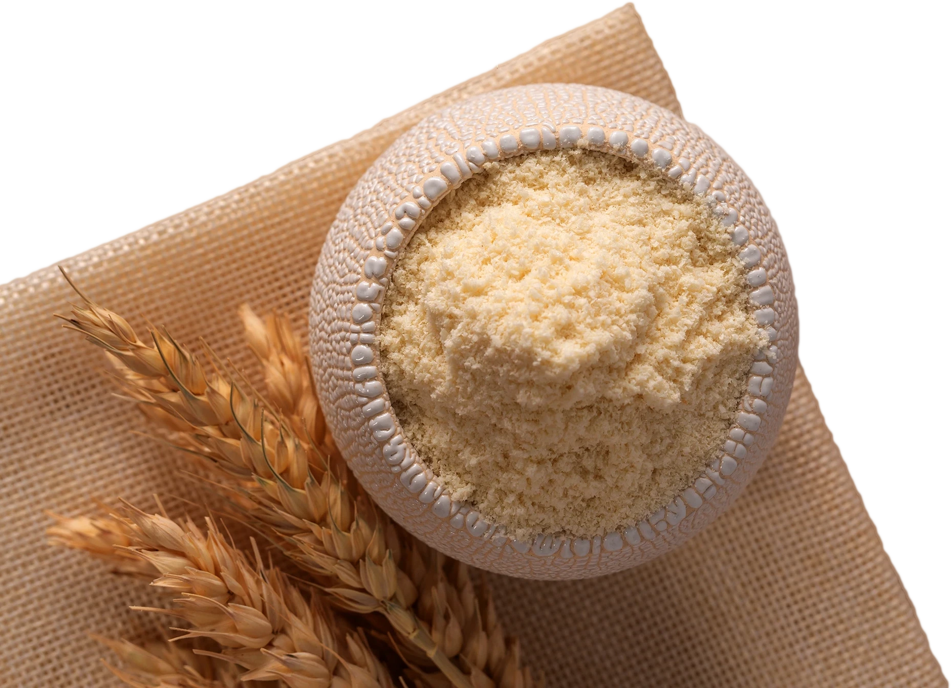 A top view of a bowl filled with fine, yellowish corn flour placed on a beige textured cloth, with several ears of dried corn lying beside it. The image highlights the texture and color of the corn flour, which is relevant for content related to corn starch, modified corn starch, and corn flour.