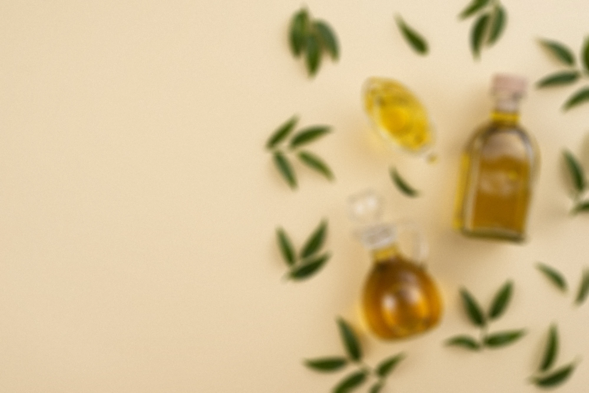 A flat lay of three bottles of essential oils and scattered leaves on a pastel yellow background.