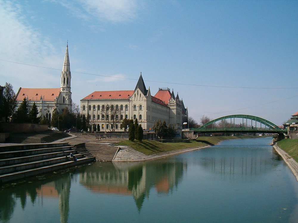 A photo of a city called Zrenjanin, river with a church and a castle on the left bank and a bridge in the background.